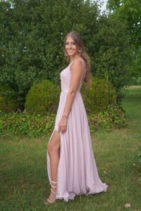 A woman wearing a long, elegant light pink dress posing next to a green manicured hedge