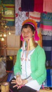 A smiling Kayan woman with brass neck rings wearing a bright green top.