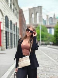 A woman wearing a black jacket and a pink top walking down a city street