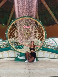 A woman sitting inside a large, decorative circular hoop installation over the water.