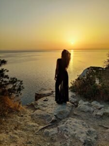 Silhouette of a person standing on a rocky cliff overlooking the ocean during a golden hour sunset