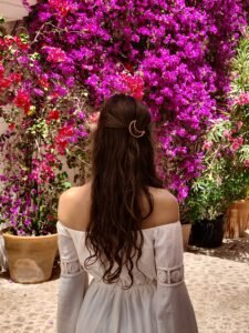 Back view of a woman with long brown hair in a white dress standing before pink bougainvillea flowers