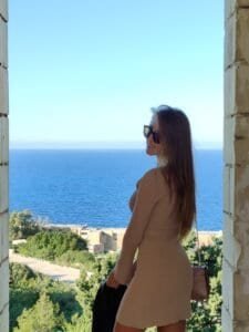 Side profile of a woman looking out at the vast blue ocean from a high stone balcony