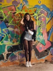 A woman leaning against a wall covered in bright, colorful street art and graffiti.
