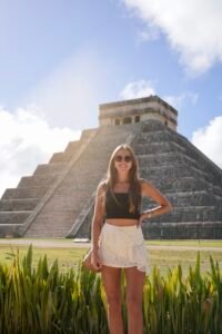 Woman posing in front of a historic Mayan pyramid under a blue sky.