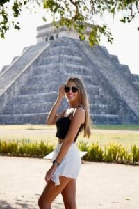 A woman in a white outfit posing in front of the Mayan pyramid (El Castillo) at Chichen Itza